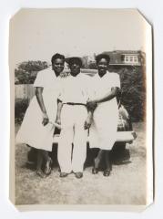 Man and two women leaning on the back of a car