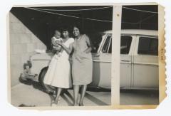 Two women and a baby leaning against a car
