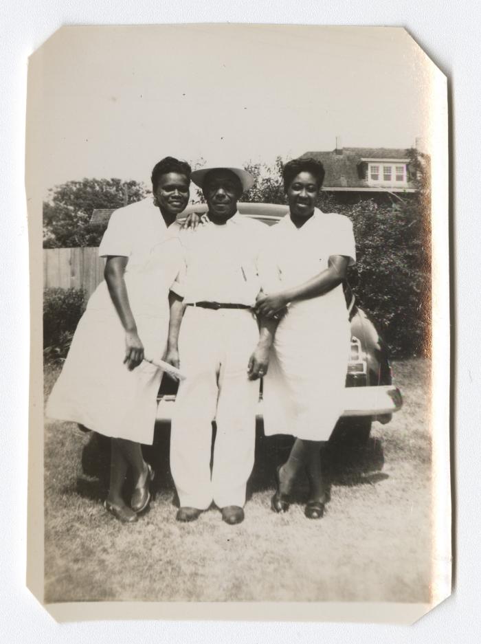 Man and two women leaning on the back of a car