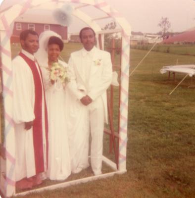 Bride, groom, and officiant standing under wedding arch