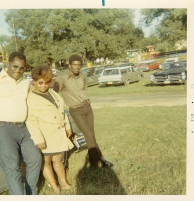 Two men and a woman leaning against a car