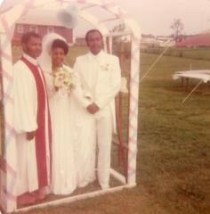 Bride, groom, and officiant standing under wedding arch