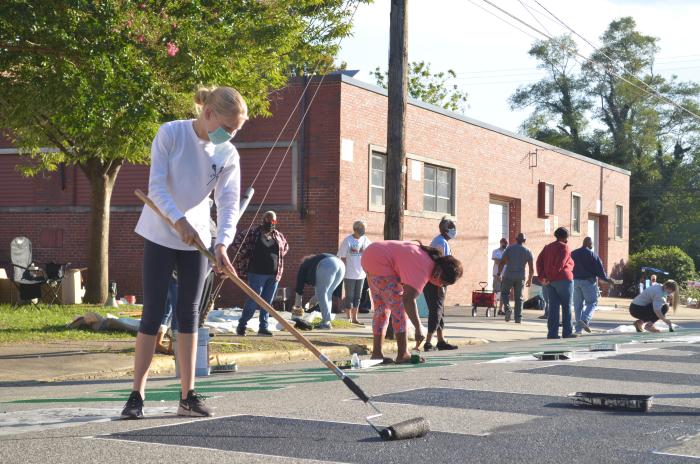 Young woman painting a black letter "H" for the Black Lives Matter street mural