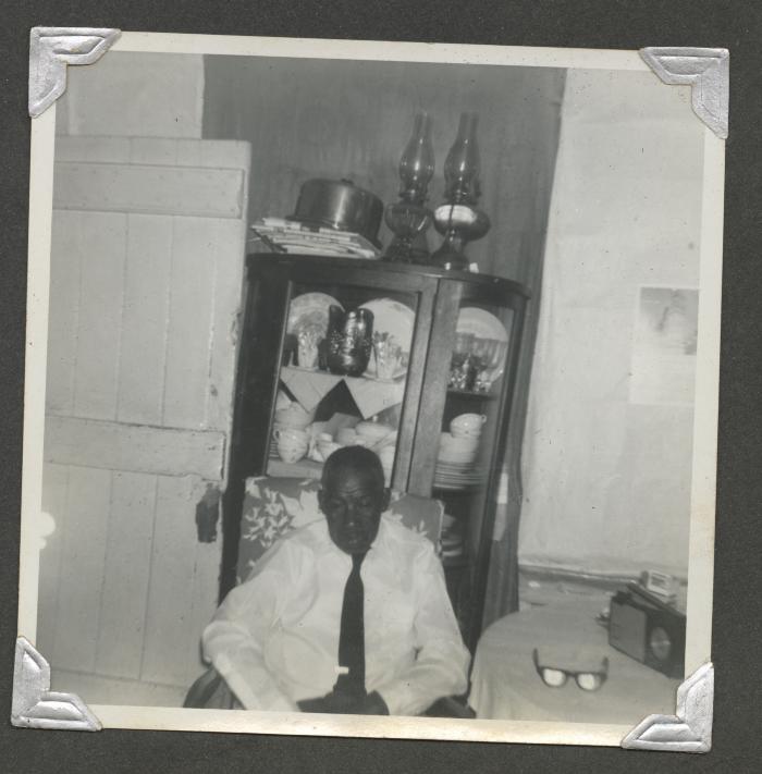 An older man sitting in front of a China cabinet