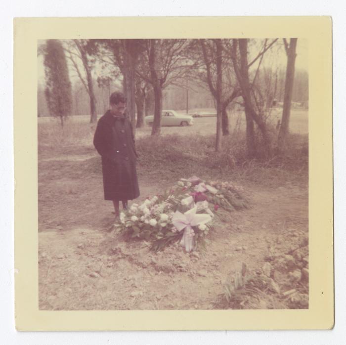 A woman standing next to a grave covered in flowers