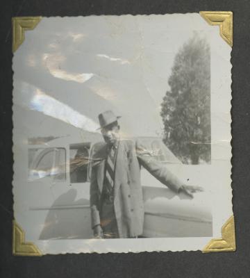 A man in a suit and hat leaning on a car