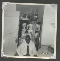 An older man sitting in front of a China cabinet