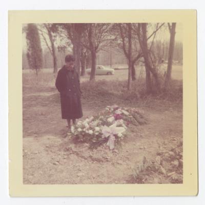 A woman standing next to a grave covered in flowers