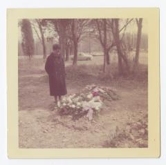 A woman standing next to a grave covered in flowers