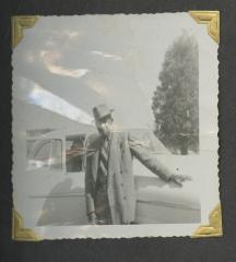 A man in a suit and hat leaning on a car
