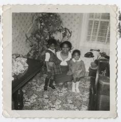 Black and white photo of a woman with two girls in front of a Christmas tree