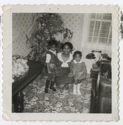 Black and white photo of a woman with two girls in front of a Christmas tree