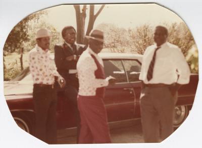 Four Formally Dressed Men Standing Around a Car